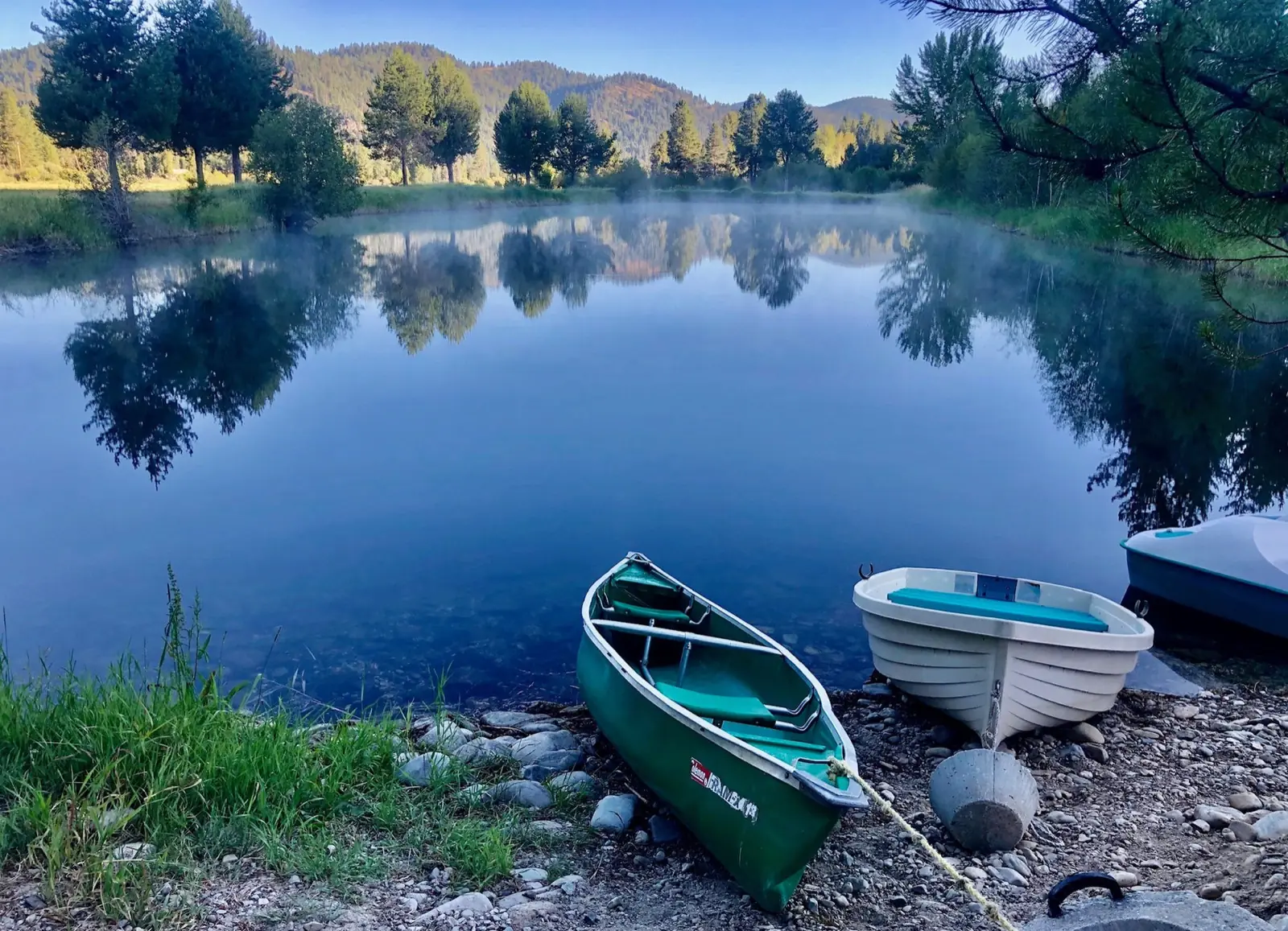 A canoe and row boat pulled up on the shore of the trout pond
