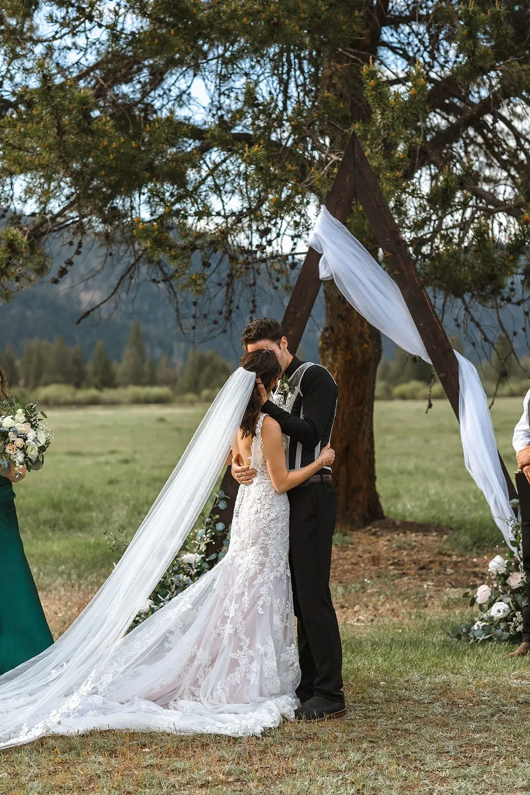 A bride and groom kissing under a big pine draped in white fabric after their ceremony