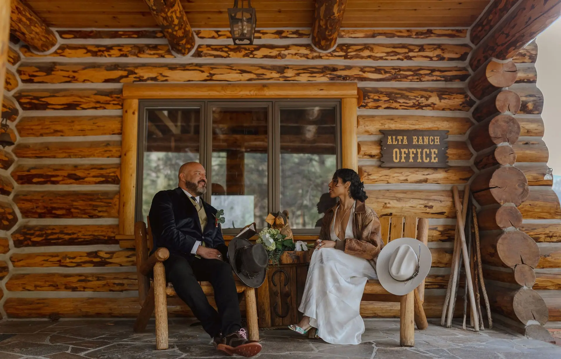A couple sitting on the porch of the log ranch office at Alta Ranch