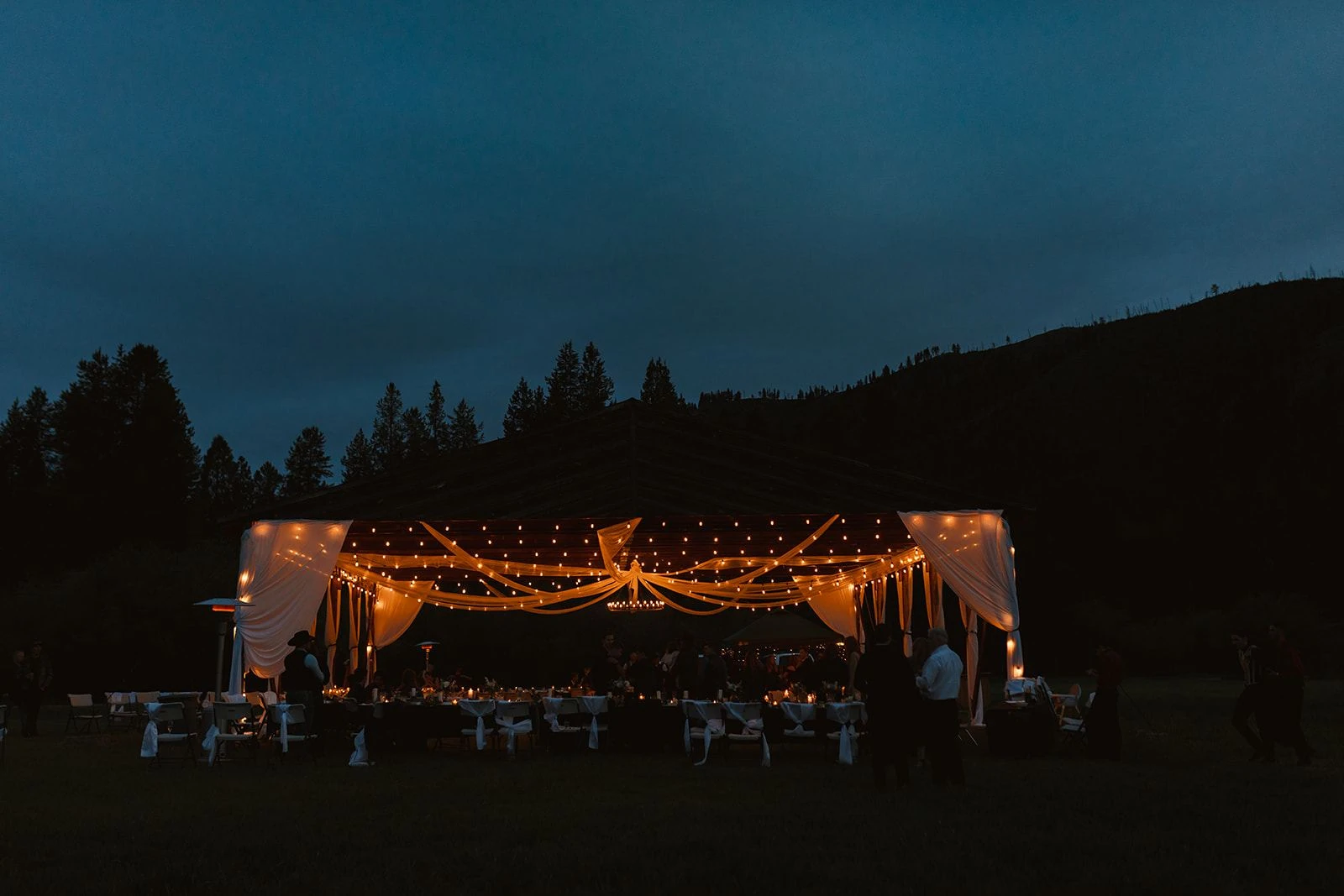 The historic hangar glowing with string lights at blue hour during a wedding reception