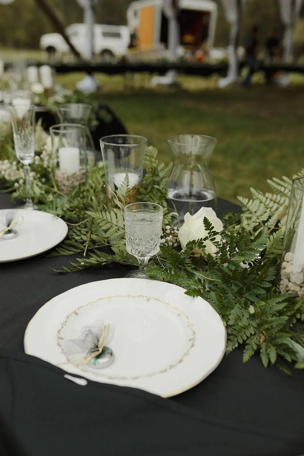 A reception table set with white plates and greenery